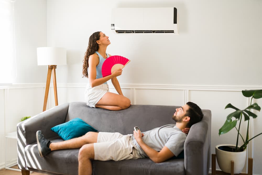 https://accutempaz.com/wp-content/uploads/2023/06/a-couple-sitting-on-the-coach-woman-holding-a-handheld-fan-fanning-herself-next-to-AC-unit.jpg